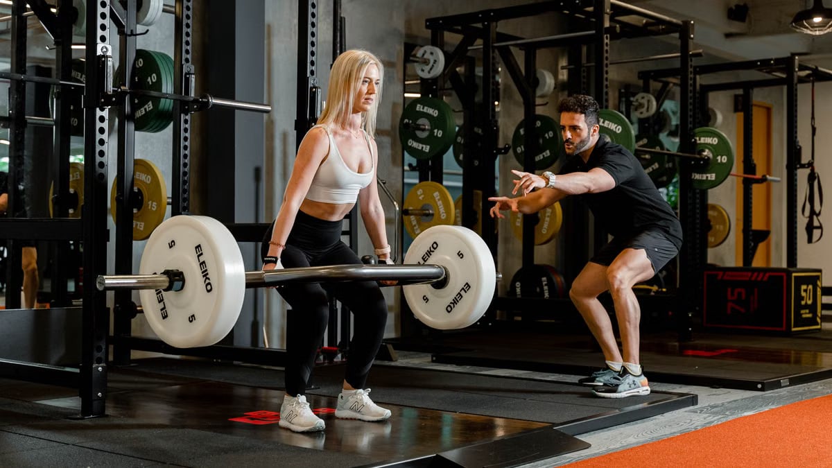 Woman lifting weights under trainer's guidance in Singapore gym, focusing on strength training.